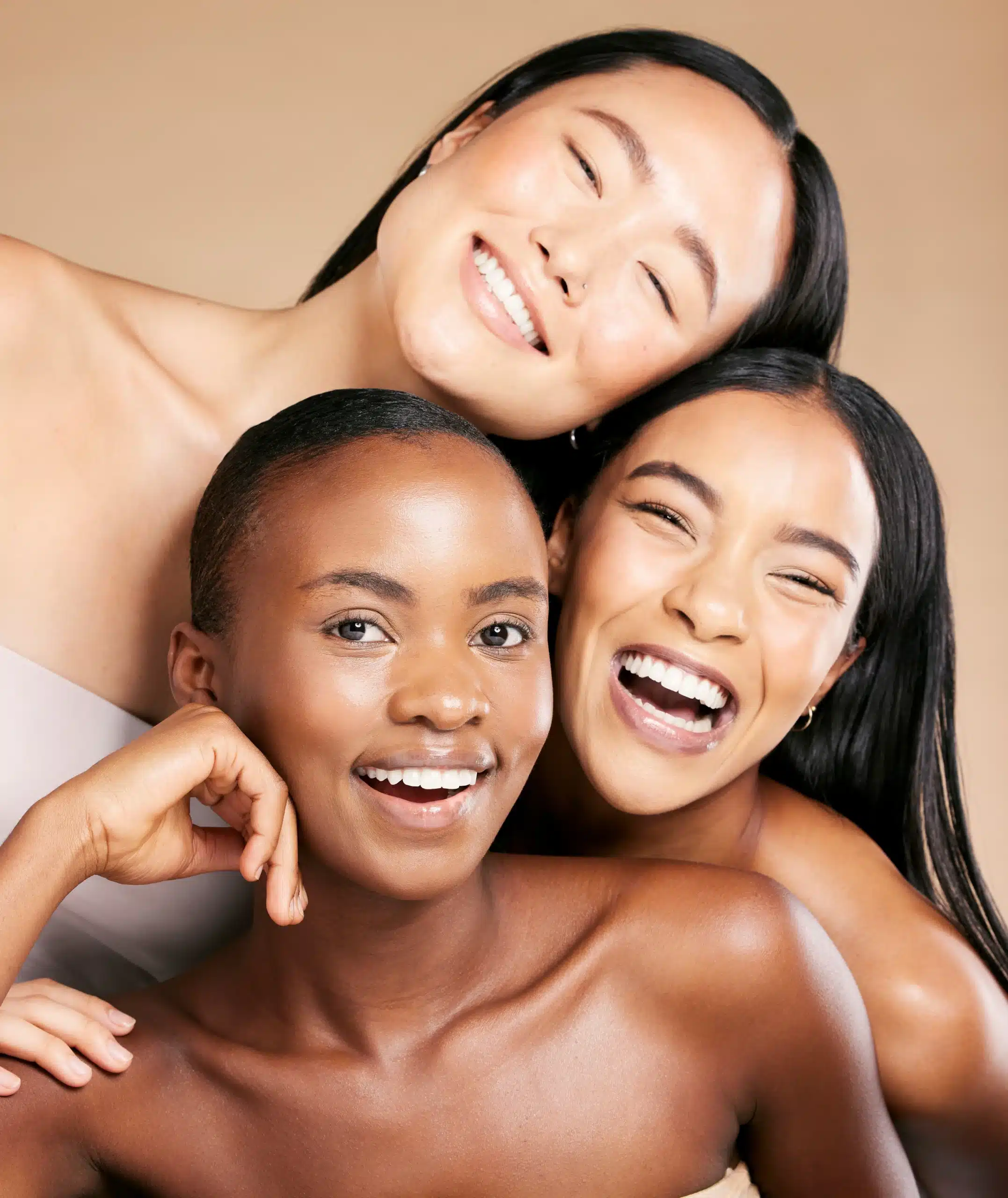 Three individuals with diverse skin tones and elegant hairstyles pose closely togetherat Well in Montclair for Emsella in Montclair, NJ.