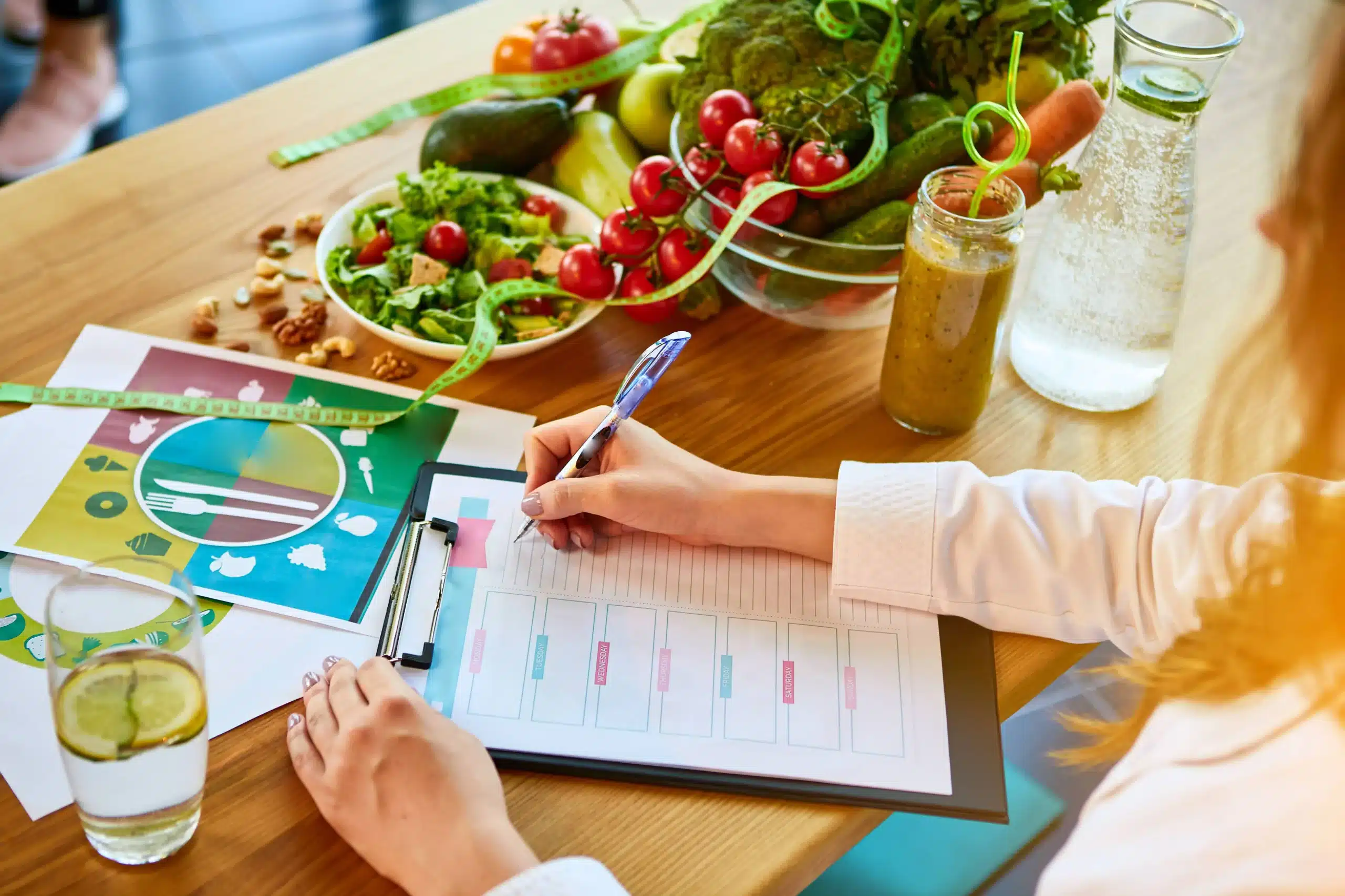 Woman dietitian working on a diet plan sitting with different healthy food ingredients in the background. Weight loss and right nutrition counseling at Well in Montclair in Montclair, NJ.