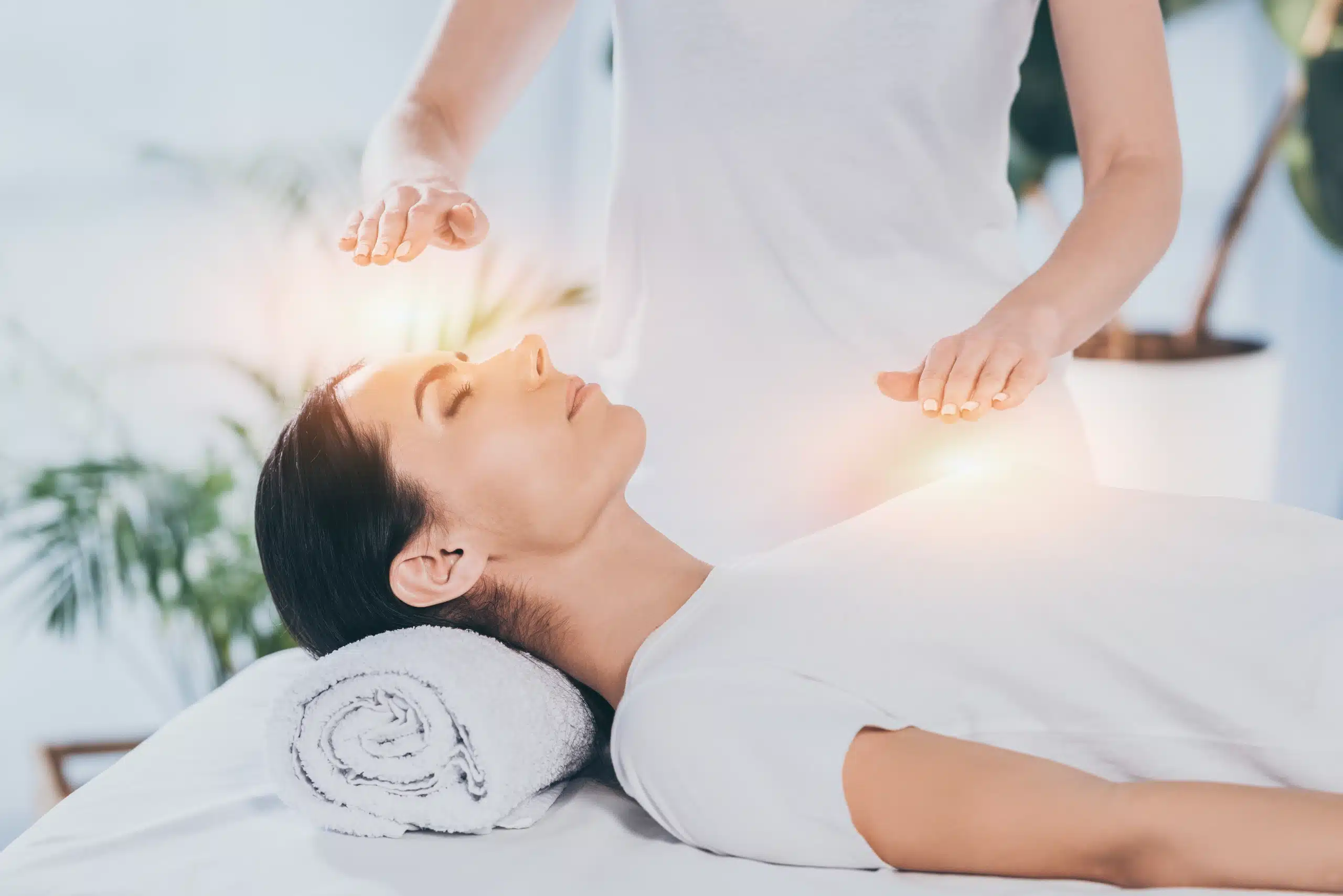 A practitioner doing reiki healing treatment with hands hovering above a client lying on a massage table at Well in Montclair for Emsella in Montclair, NJ.