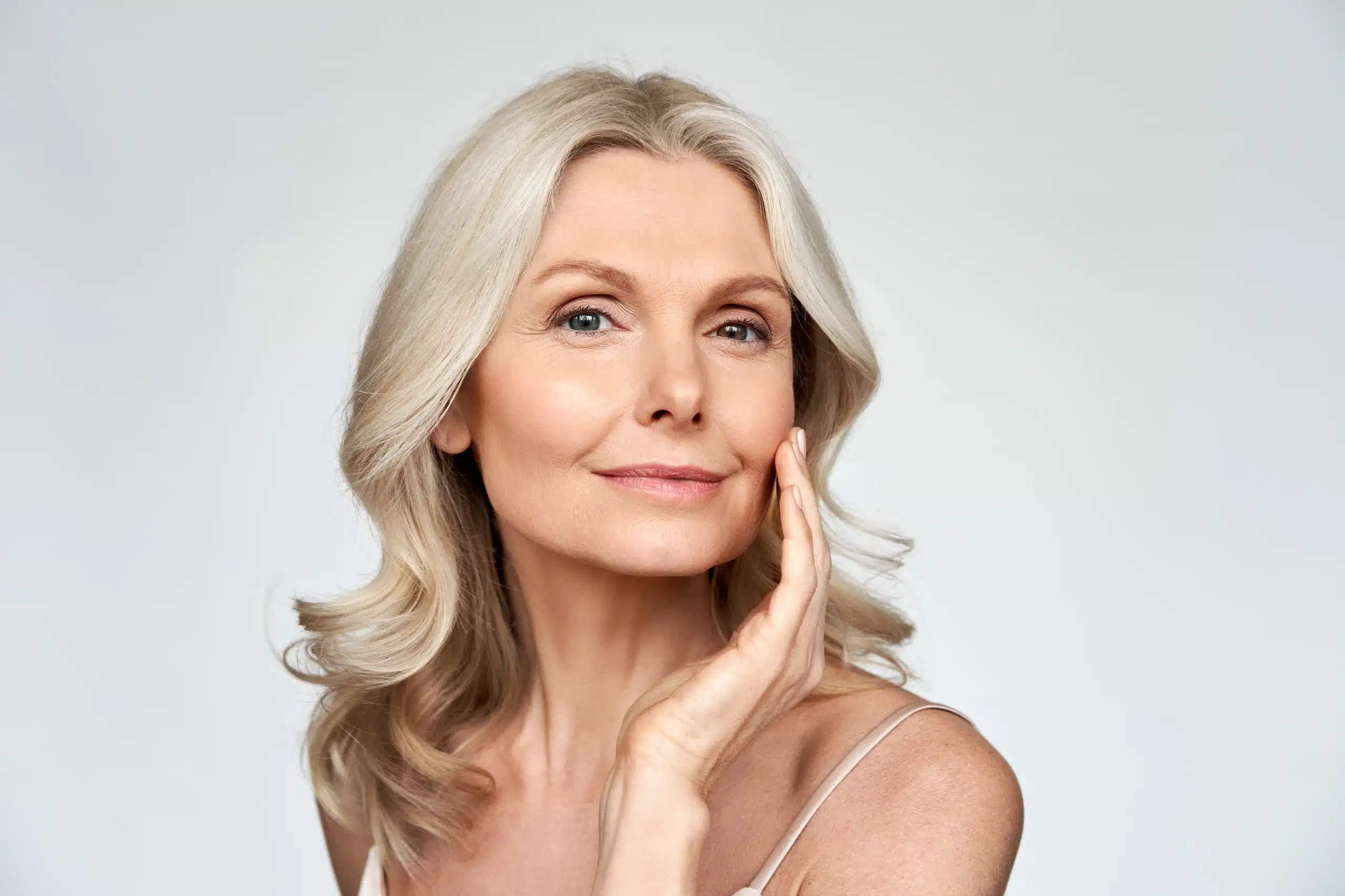 A mature woman with smooth, radiant skin and silver-blonde hair touches her face gently, showcasing Exion before and after results at Well in Montclair in Montclair, New Jersey.